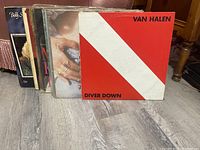 Photo showing the front of 12 vinyl record albums stacked, Van Halen Diver Down album visible in front with red and white diagonal cover