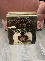 Front view of Steppenwolf Live vinyl record at the front of the stack with other records behind, showing wear and aging on the cover.