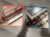 Two Beatles vinyl record albums side by side on the floor with visible wear on covers