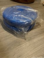 Two blue inflatable balance discs stacked and wrapped in plastic, placed on floor
