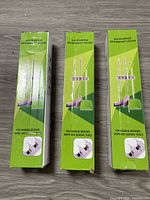 Photo of three new, boxed multipurpose broom/mop holders with green and white packaging showing product usage images and labeling.