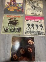 Top view of 5 Beatles vinyl record covers arranged on floor showing colorful Yellow Submarine cover, Revolver illustrated cover, Beatles '65 photo cover, Twist and Shout cover, and one with Beatles faces portrait