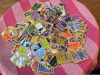 Loose Pokémon cards spread on a pink striped cloth showing a wide variety of cards, including water, psychic, grass, fire types.