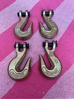 Top view of four forged RB1 transport hooks on a pink cloth background, showing their shape and markings.