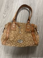 Front view of Fossil handbag showing patterned fabric, leather trim, handles, and metal logo plate.