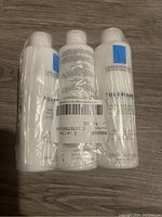 Three sealed white bottles of La Roche-Posay Toleriane Dermo-Cleanser in plastic packaging.