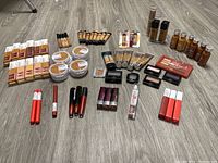 Photo showing array of foundations, powders, concealers, lipsticks, and makeup sticks laid out on floor.