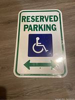 Photo of metal reserved parking sign with handicap symbol and bidirectional arrow shown on a wooden floor.