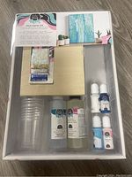 Front view of resin starter kit showing included components in tray: resin, hardener, colorants, wooden panel, plastic cups, glitter packet.