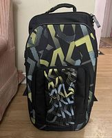 Soft suitcase upright against wall showing overall patterned exterior, top handle, and front pocket.