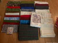 Large assortment of folded fabric pieces on wooden floor, showing variety in color, pattern, and texture.