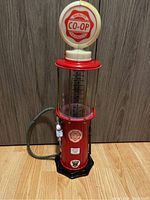 Front view of vintage CO-OP style gas pump model showing red body, clear measurement cylinder, and white topped globe logo light.