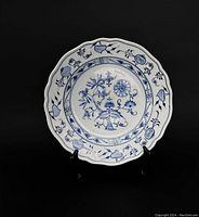 Front view of antique blue onion decorated porcelain soup plate on black background with stand.
