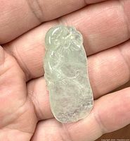Front side of the translucent light green jade pendant showing floral and natural motif carvings held in hand.