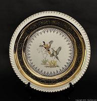 Front view of round vintage plate with bird illustration and gold ornate border.