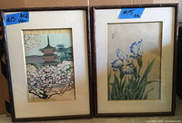 Pair of two framed Japanese prints, one showing a pagoda with cherry blossoms and the other with blue iris flowers, each with matching wooden bamboo-style frames and mats.