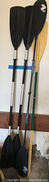 4 kayaking paddles: one pair with black blades and aluminum shafts, two singles including one with wooden shaft and tan blades.