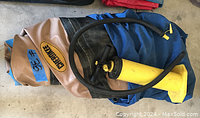Folded Cherokee inflatable raft in tan and blue material with the Cherokee logo, accompanied by a yellow hand pump with black hose and handles laid on top.