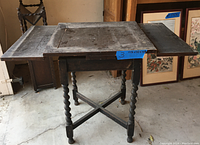 Front view of the wooden extendable side table with two leaves folded out on both sides, barley twist legs, and visible wear on the tabletop.