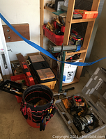 Overview of wooden shelving unit, tool chests, carryalls, and red/black tool bag with hand tools.