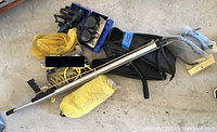 Photo shows snorkeling gear including mask, fins, a diving cutter attached to a thigh holster, a metallic speargun with spear shaft, and a yellow mesh bag on concrete floor.