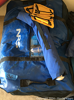 Blue NRS rafting bag with black straps, partially showing contents through clear window, with rolled item secured on top.