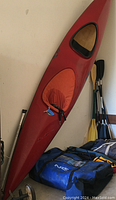 Red Old Town Canoe tandem kayak with two cockpits, orange skirts (one missing), positioned vertically on wall with pillows and paddles around.