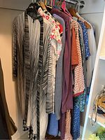 Photo showing a variety of tops and dresses on hangers, including a black and white striped garment and floral patterned one.