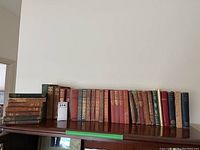 Wide view of entire book collection on wooden table showing about 30 books in various bindings and colors.