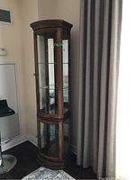 Tall wooden display cabinet shown closed to view overall structure, curved glass front and wooden frame.