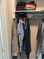 Wide view of hanging clothes and folded clothing on shelf showing various tops and pants.