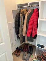 Five coats hanging on a rail inside a closet, visible from left to right: black puffer jacket, leopard print faux fur coat, cream colored spring coat, dark wool boucle coat, and red ski jacket. On the floor below are several pairs of women's boots and shoes in various colors including brown and gray.
