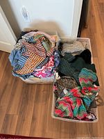 Two large plastic bins filled with assorted ladies scarves in various fabrics and colors including knitted and printed silk scarves.