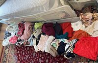 Assorted lounge wear including sweaters, tops, housecoats laid out on a patterned carpet next to a storage bin