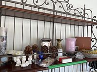 Overall front view of shelf displaying assorted collectibles: ceramic angels, brass vase, pink glass lamp, coasters, candle holders, decorative wooden pieces