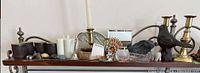 Wide view showing various collectibles arranged on a shelf, including brass candle holders, pottery cups, small figurines, and decorative items.