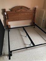 Queen size bed frame showing oak wood headboard with carved design and black metal frame base without mattress.