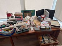 Full view of office supplies and small office equipment on wooden desk showing various containers, paper stacks, Canon Selphy printer box, and assorted items.