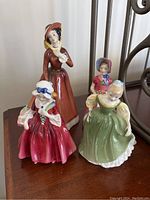 Four Royal Doulton figurines displayed on a wood surface, showing varied dresses and colors.