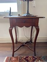 Front view of the wooden side table showing the single drawer, Queen Anne legs, and crossed stringers.