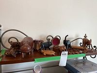 Wide view of small wooden animal figurines and other souvenir items on a wooden shelf showing hippo, elephants, lion, turtle, yak, carved wooden items and necklace.