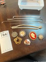 Photo of two sterling chains, pearl bracelet with decorative clasp, cameo brooch, mother of pearl brooch, crown-shaped brooch, floral engraved silver-tone brooch, starburst costume brooch with pearls, and a round engraved pendant.