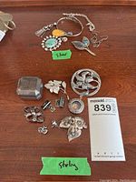 Overview of sterling and silver jewelry lot including pendants, pins, bracelets, earrings, and cufflinks on wooden surface.