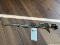 Full view of dagger laid flat on wood floor showing wavy blade profile and handle.