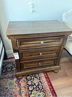 Front view of one walnut veneer night stand showing three closed drawers and round metal knobs