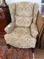 Front view of beige and teal paisley upholstered wingback chair with lumbar cushion on seat