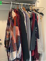 Photo showing a variety of women's sweaters and cardigans on hangers, including colorful striped knit cardigan with patchwork design, other muted solid and patterned sweaters, various fabric textures.