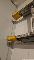 Close-up of worn wooden side with yellow plastic foot caps on the bottom of the ladder.