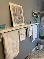 White textured bath towels hanging on a rack with floral artwork and vase in background.