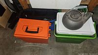 Two Coleman coolers, one green and white, one orange, with a vintage metal kettle on top of the green cooler